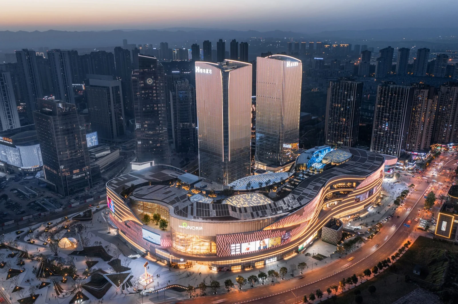 Evening aerial view of The Ring in Chongqing, showing the illuminated retail podium, rooftop garden and office towers.